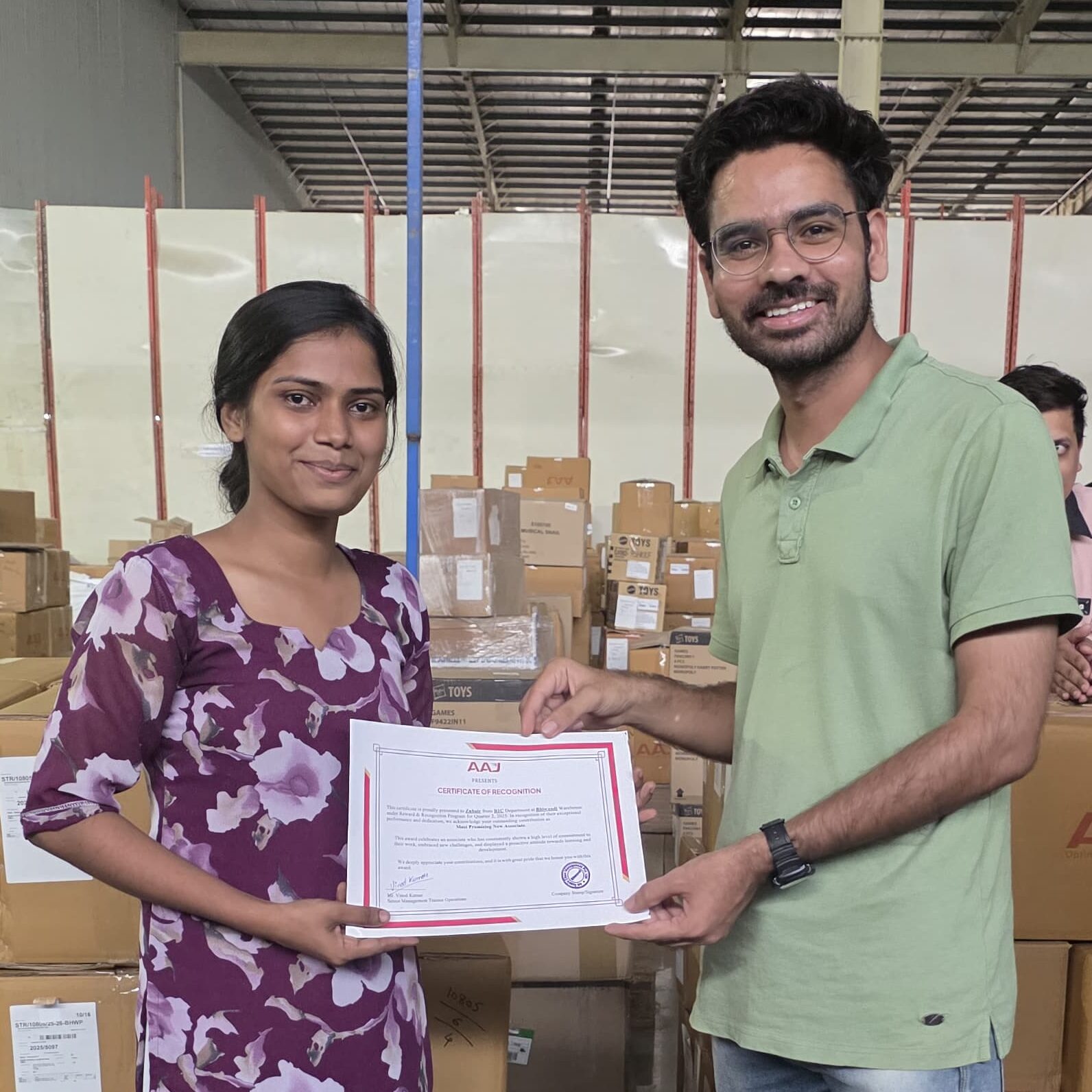 A jubilant AAJ SCM team member is presented with an award certificate by a colleague, celebrating their dedication during the recent recognition ceremony.